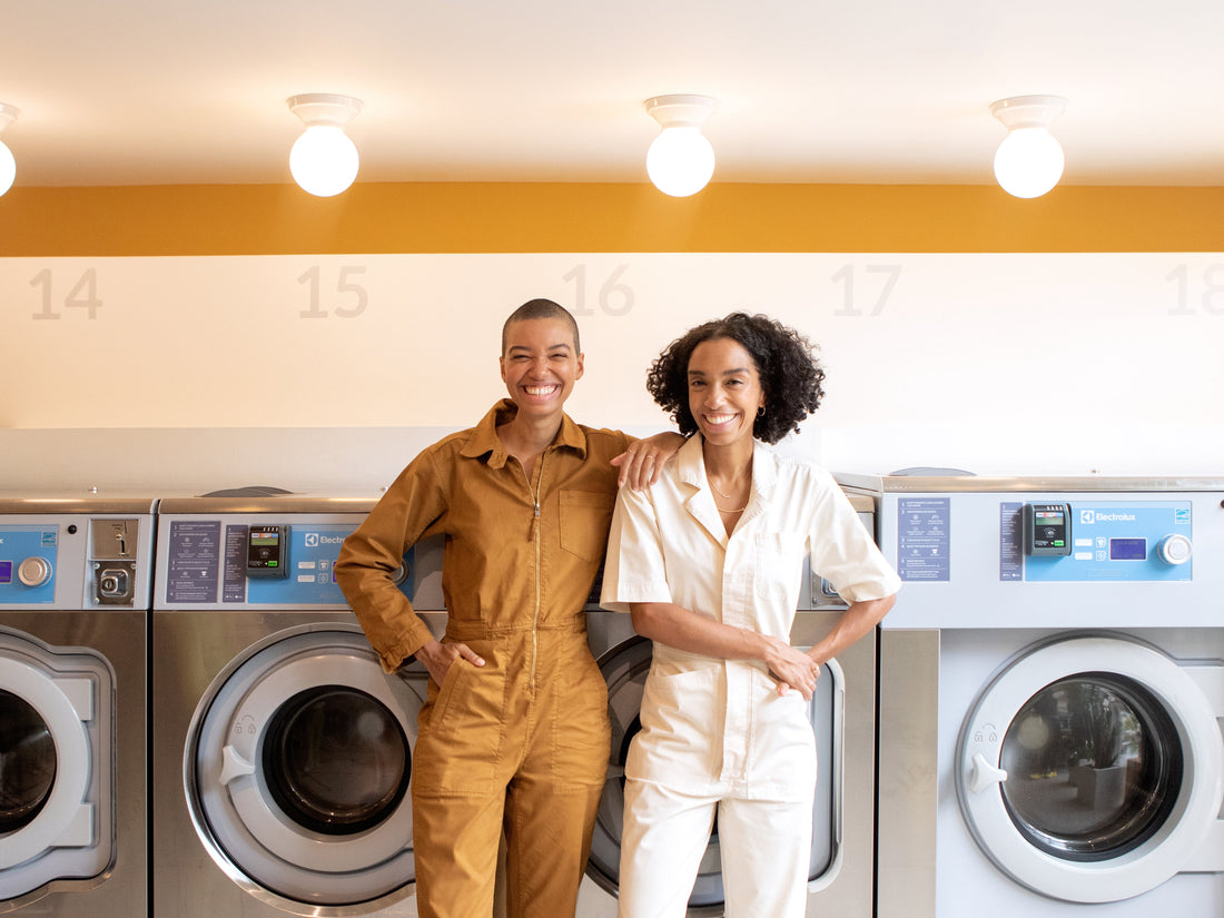 Corinna and Theresa Williams wear jumpsuits and smile for the camera at Celsious laundromat