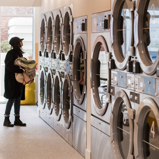 A college student in a cap holding laundry at a laundromat
