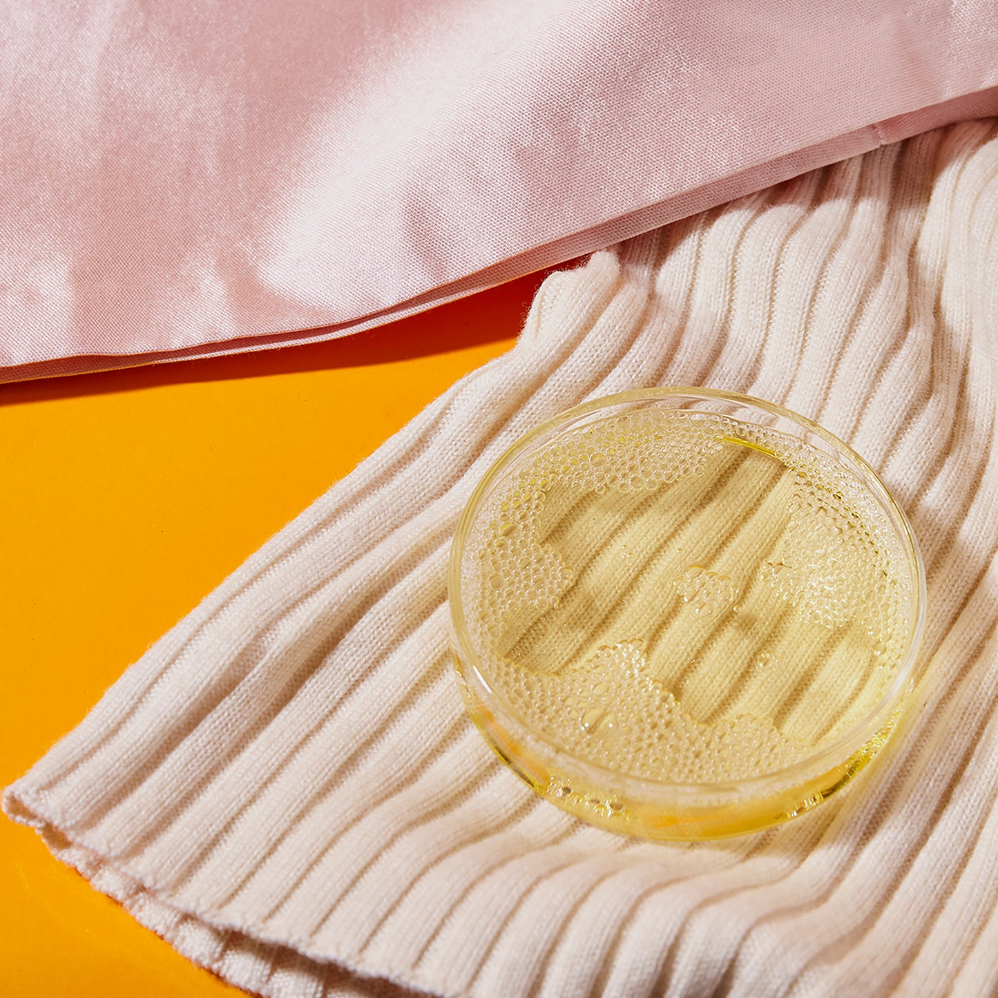 A dish filled with olive liquid detergent beside wool and silk fabrics