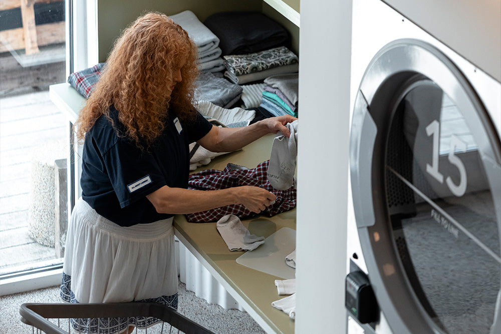 A woman folds socks and clothes on a sage green table