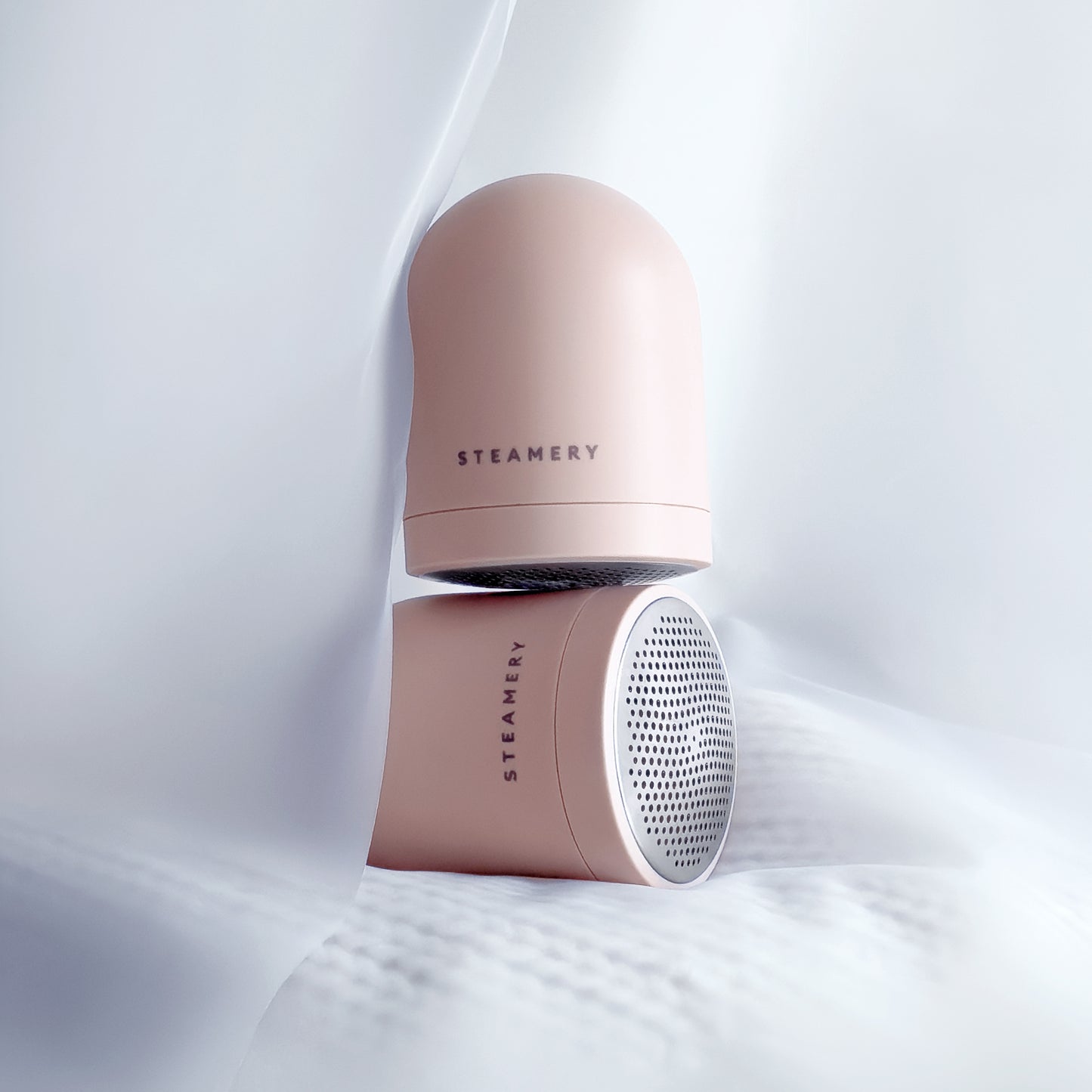 Two rose pink fabric shavers stacked on top of each other and enveloped in soft white fabric