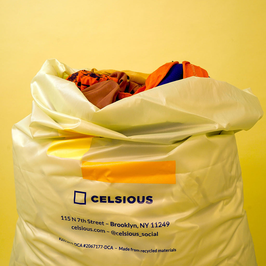A yellow Celsious laundry bag with fluffy laundry peeking out of the top