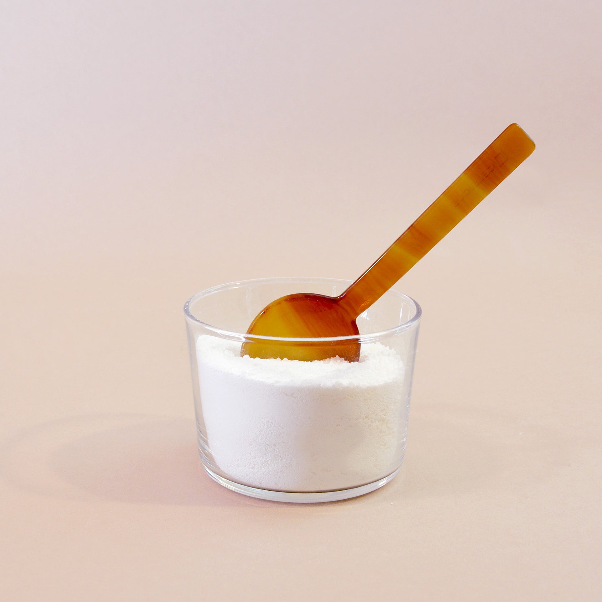 A sunset orange and yellow measuring spoon perched in a glass full of white laundry powder