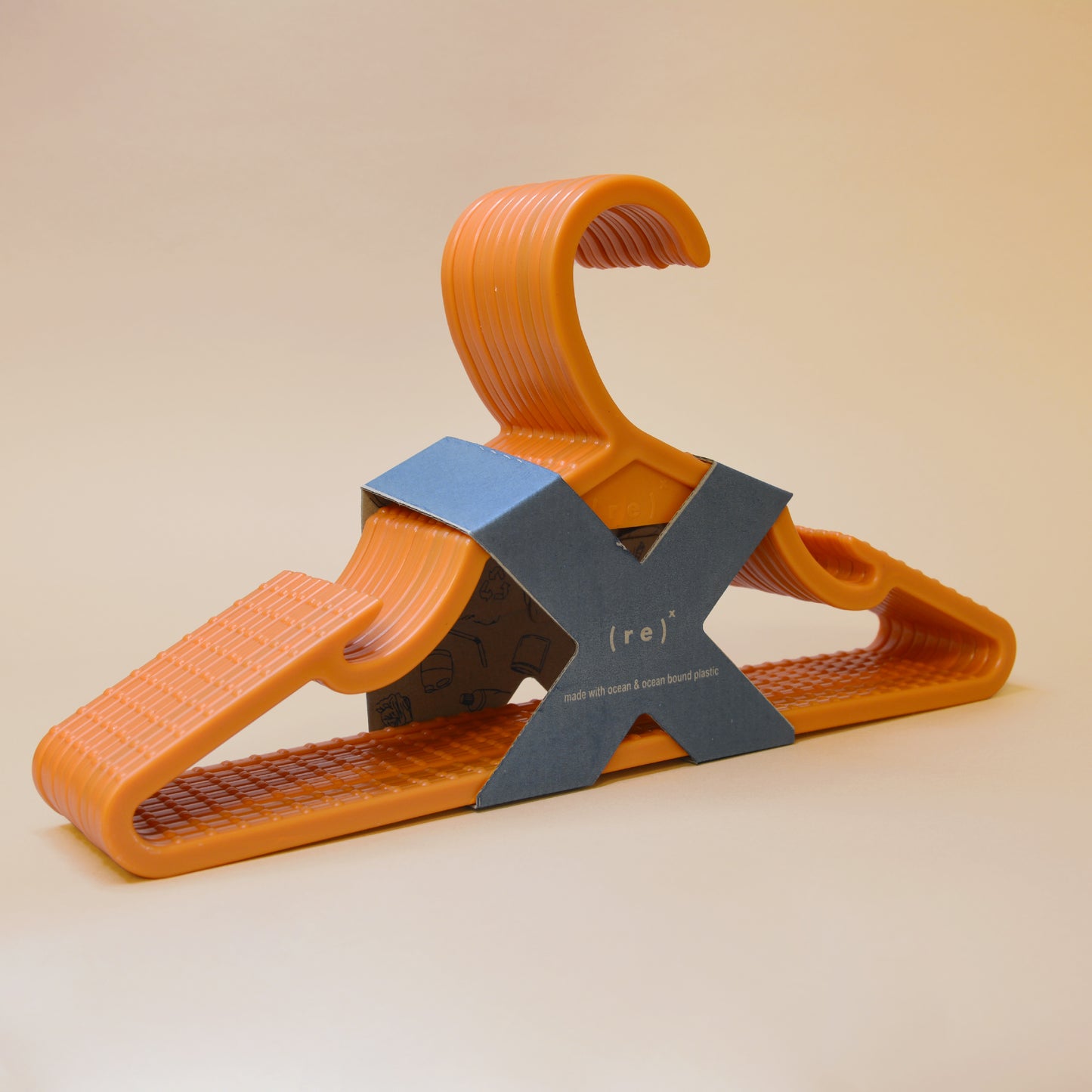 A pack of orange recycled plastic hangers with anti-slip grooves held together by X-shaped kraft paper labels