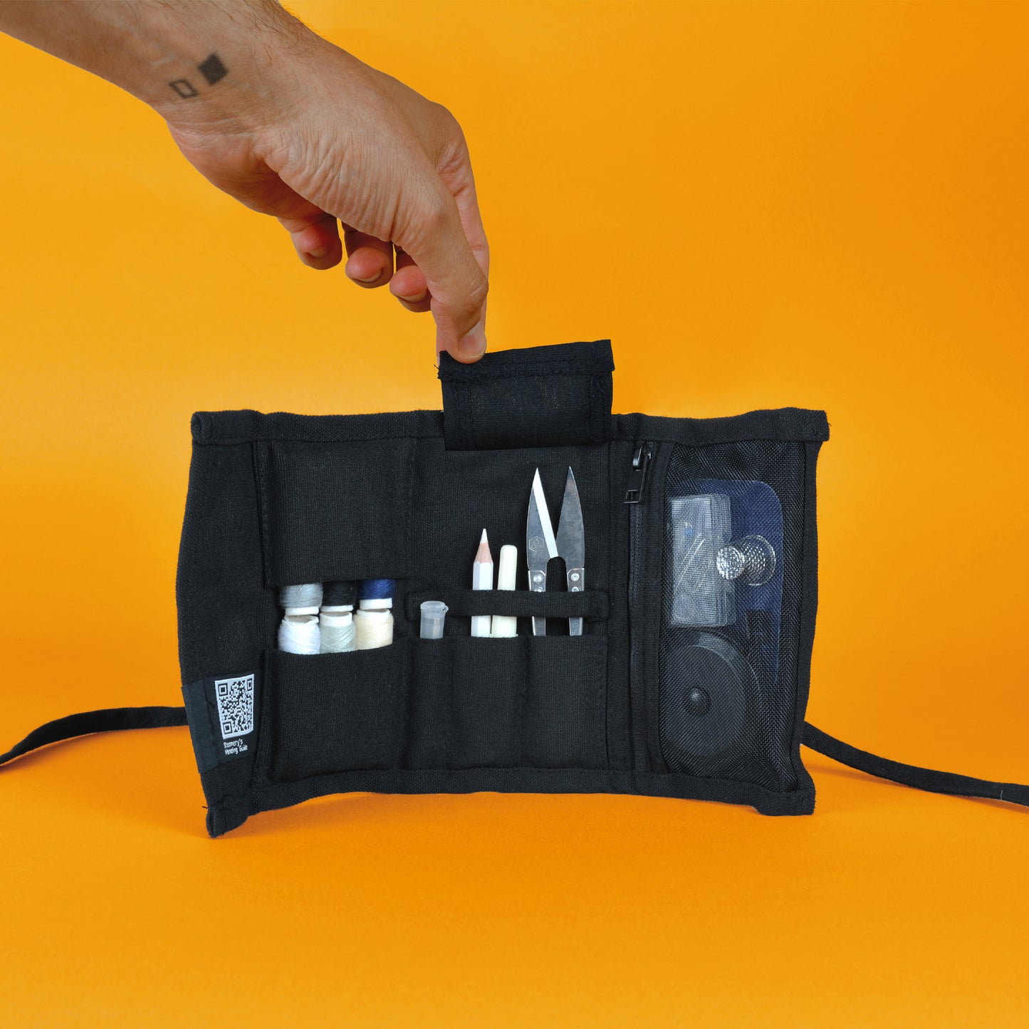 A hand lifting up a fabric flap inside the Steamery sewing kit, revealing sharp thread scissors underneath