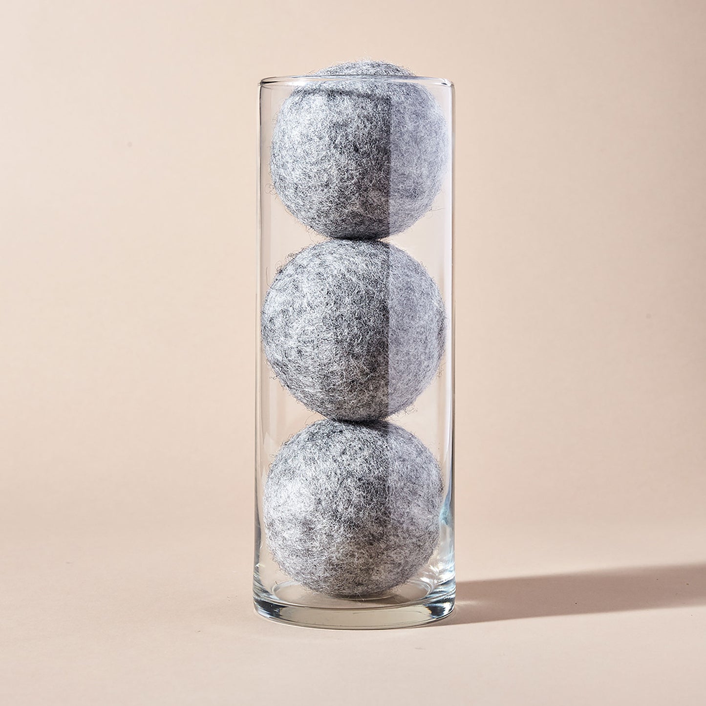 A stack of three grey wool dryer balls displayed in a tubular glass container