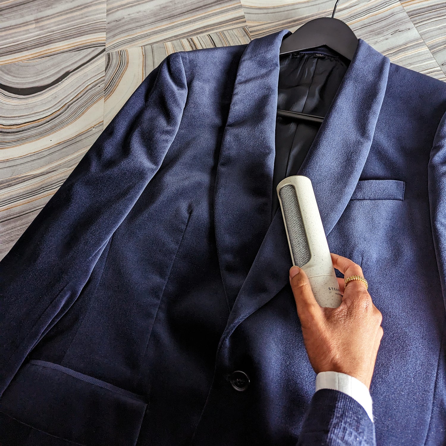 Holding a lint removing tool up to a navy blue velvet suit jacket