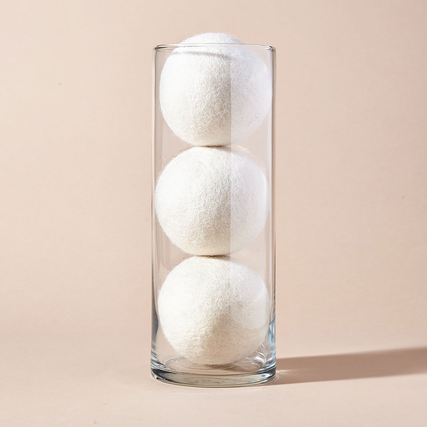 A stack of three white wool dryer balls displayed in a tubular glass container