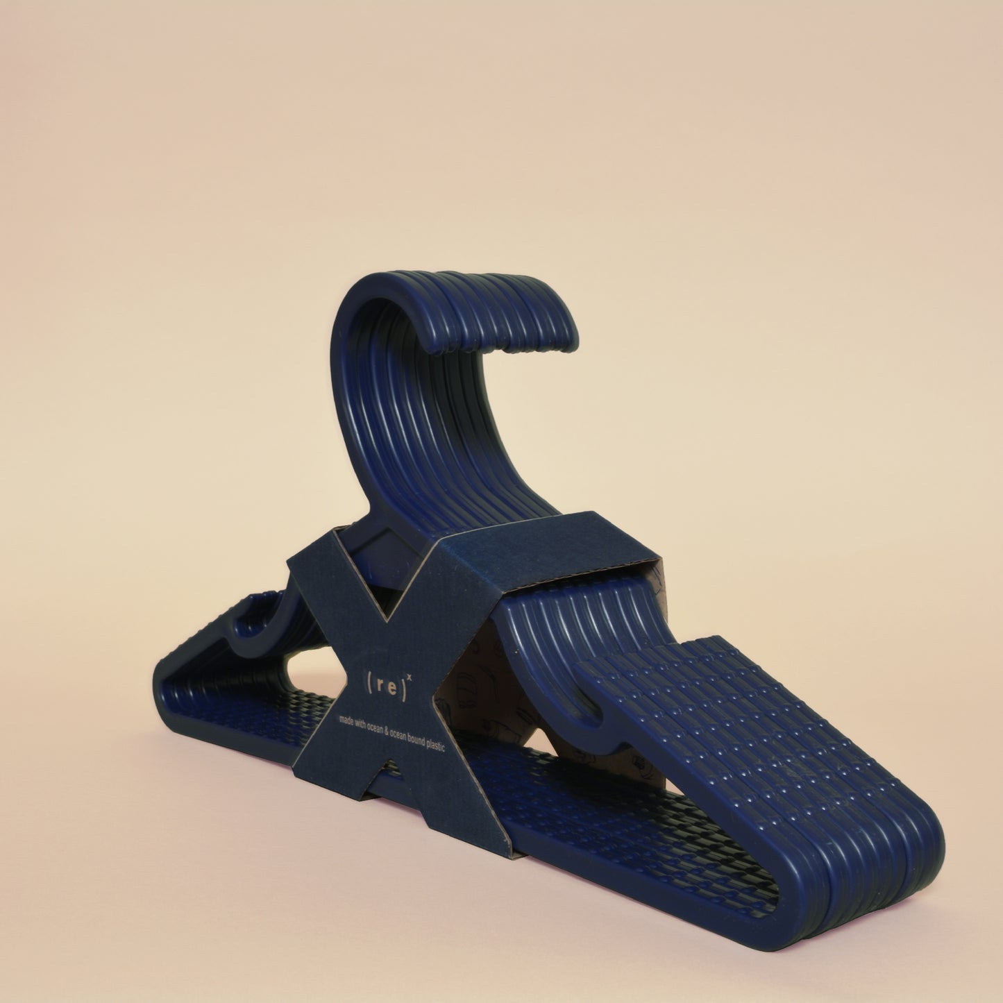 A pack of navy recycled plastic hangers with anti-slip grooves held together by X-shaped kraft paper labels