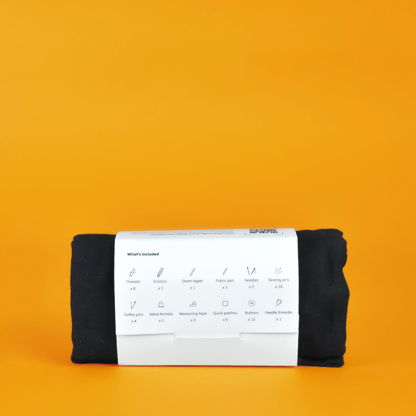 A rolled up Steamery sewing kit in a white paper sleeve, the back of which lists the contents of the kit