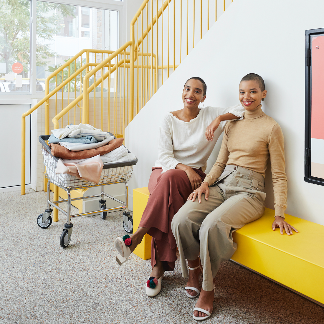 Corinna and Theresa Williams sit on a yellow bench next to a cart full of linens at Celsious