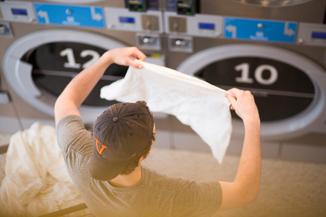 A college student wearing a baseball cap shakes out his laundry