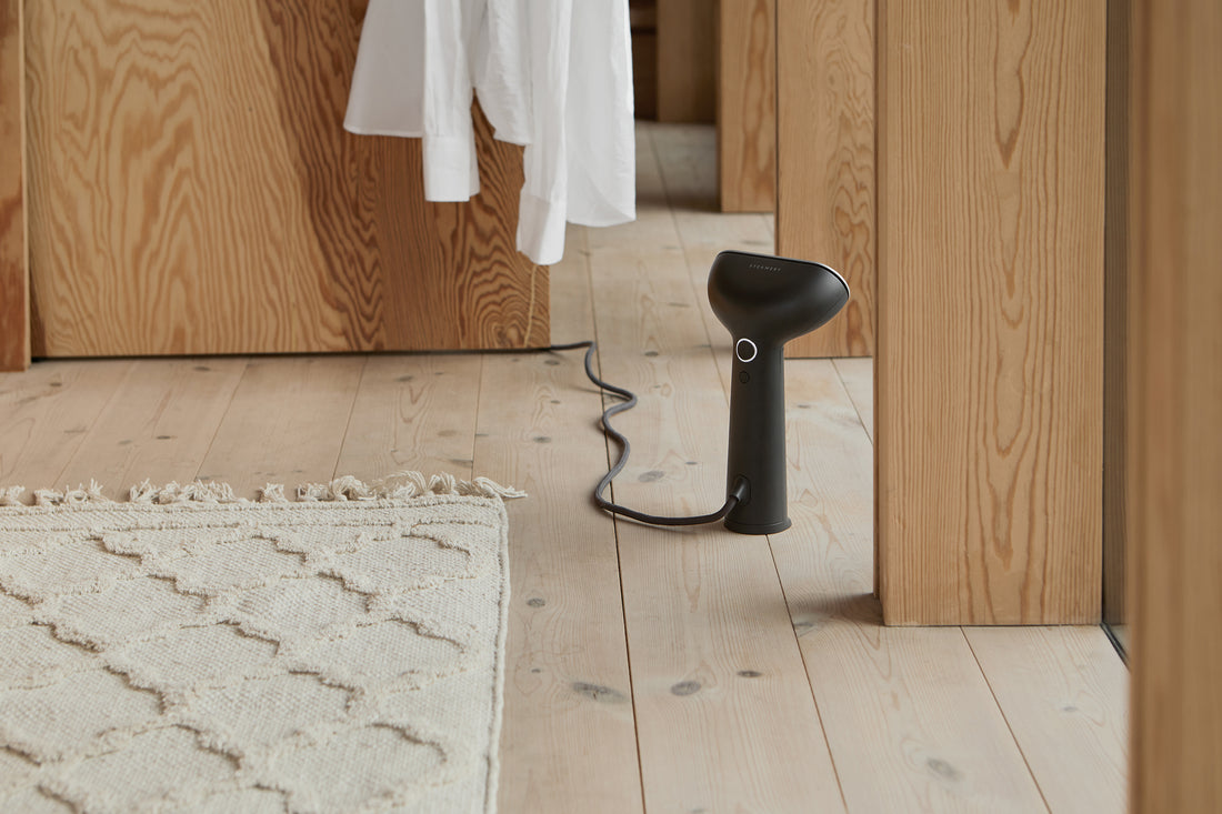 The Cirrus 3 iron steamer stands upright on the floor of a cottage; a white button down is hanging in the background