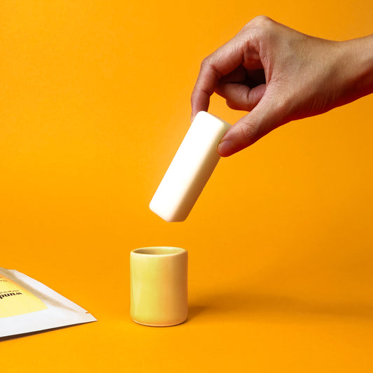 A hand places a soap stick into a butter yellow cylindrical ceramic container