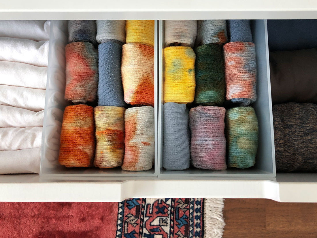 A drawer pulled open to show neat rows of expertly folded tie-dye socks, t-shirts and sweaters