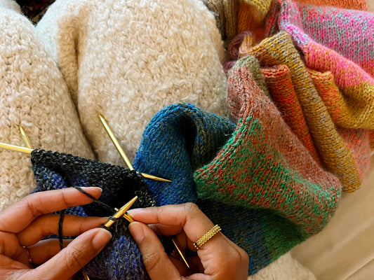 A close up of hands knitting a colorful scarf