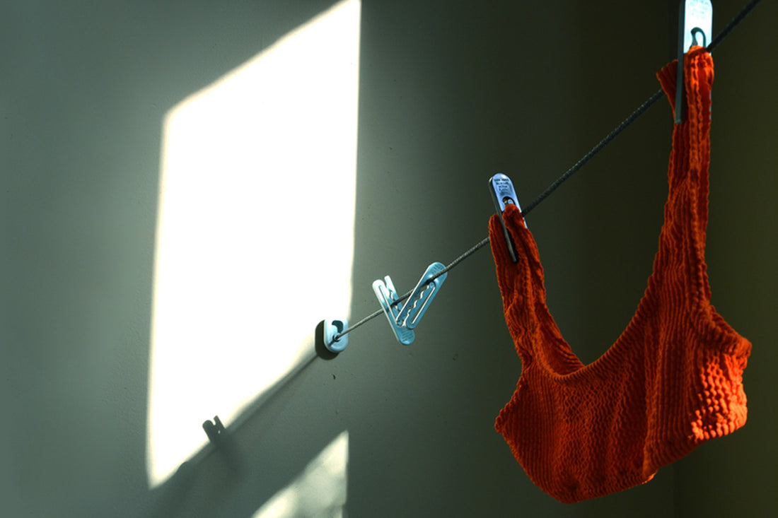An orange swimsuit top hangs from a clothesline in moody lighting