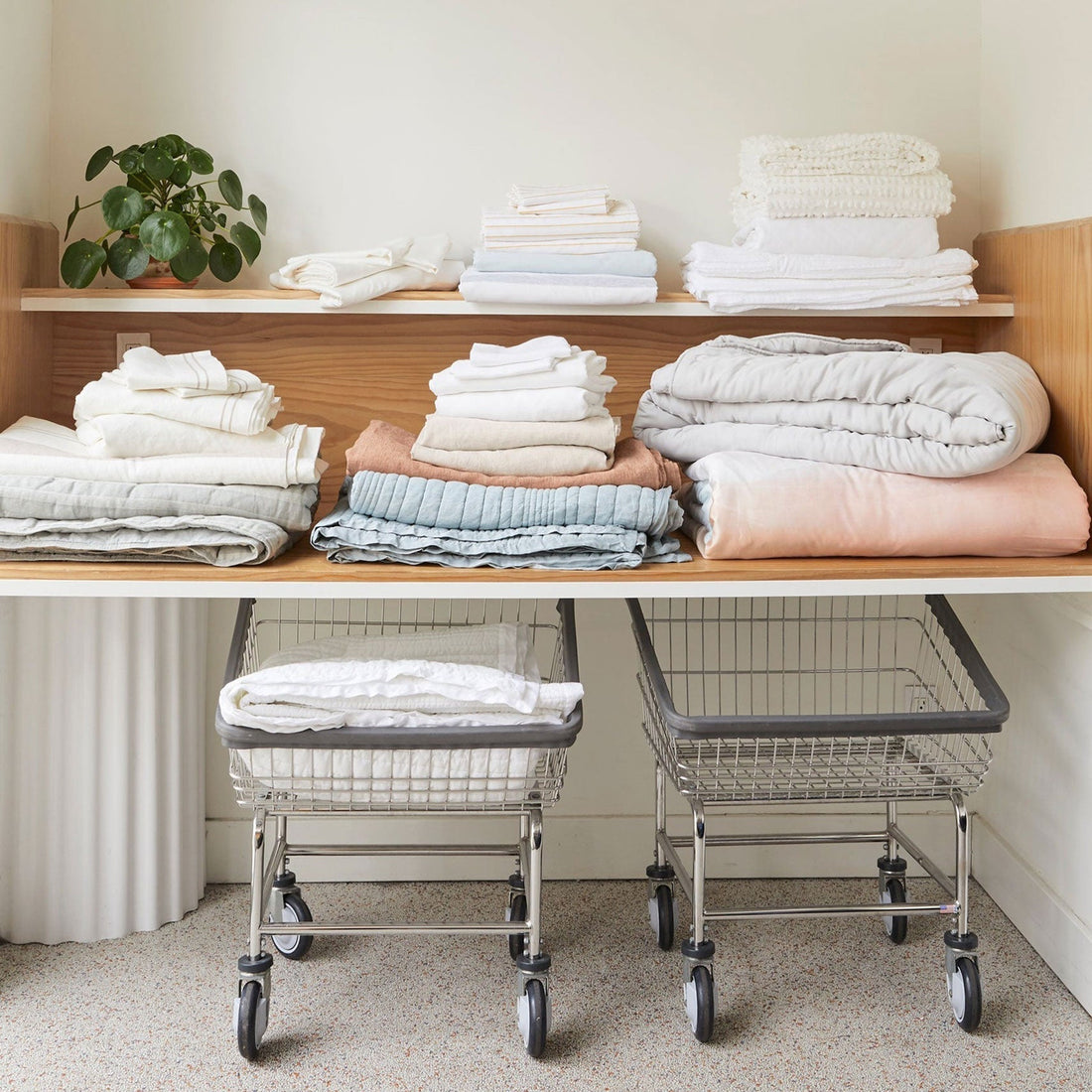 Folded stacks of fluffy bed linens on a wood folding table, and laundry carts underneath, at Celsious