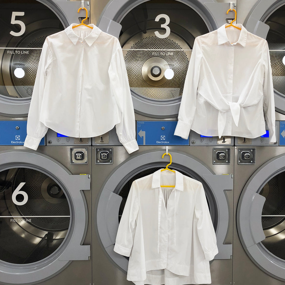 Three crisp button down white blouses hanging in front of modern dryers