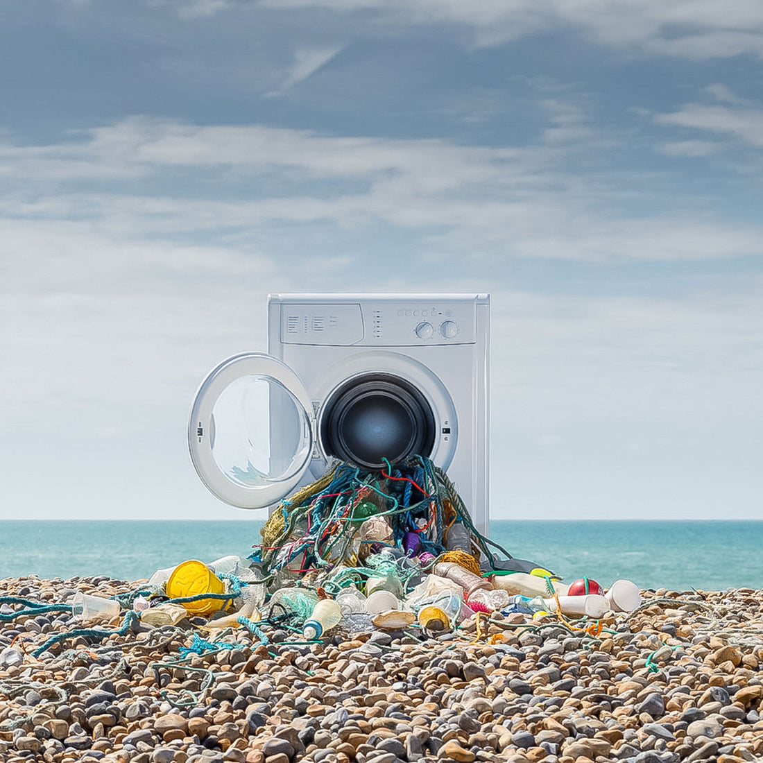 A washing machine on a pebble beach with plastic bottles and nets spilling out of the drum: an artistic interpretation of plastic pollution in our oceans