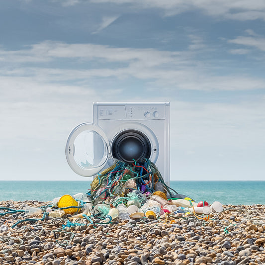 A washing machine on a pebble beach with plastic bottles and nets spilling out of the drum: an artistic interpretation of plastic pollution in our oceans