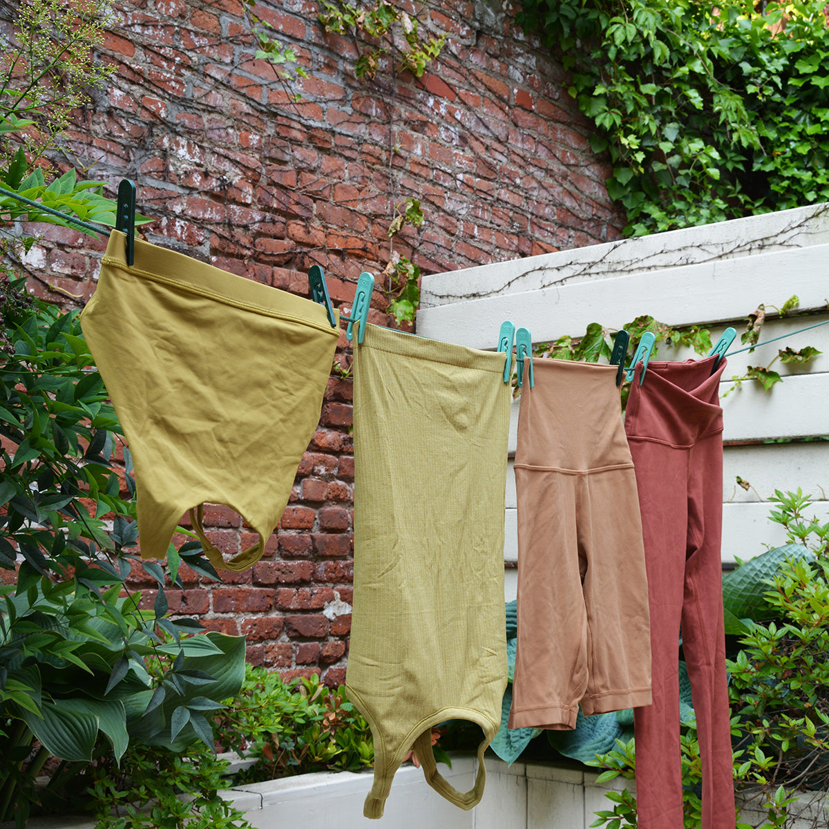 Women's yoga clothes hanging on a clothesline in a leafy backyard