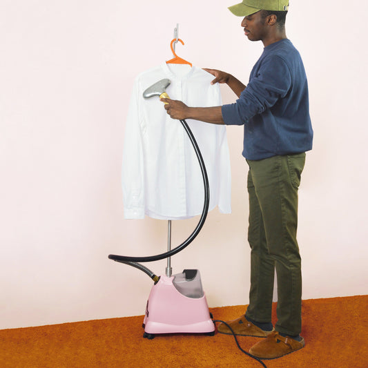A man uses a Jiffy upright steamer with a metal head to steam wrinkles out of a hanging white button down shirt