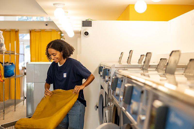 A woman smiles while folding in a tidy laundry space with yellow accents