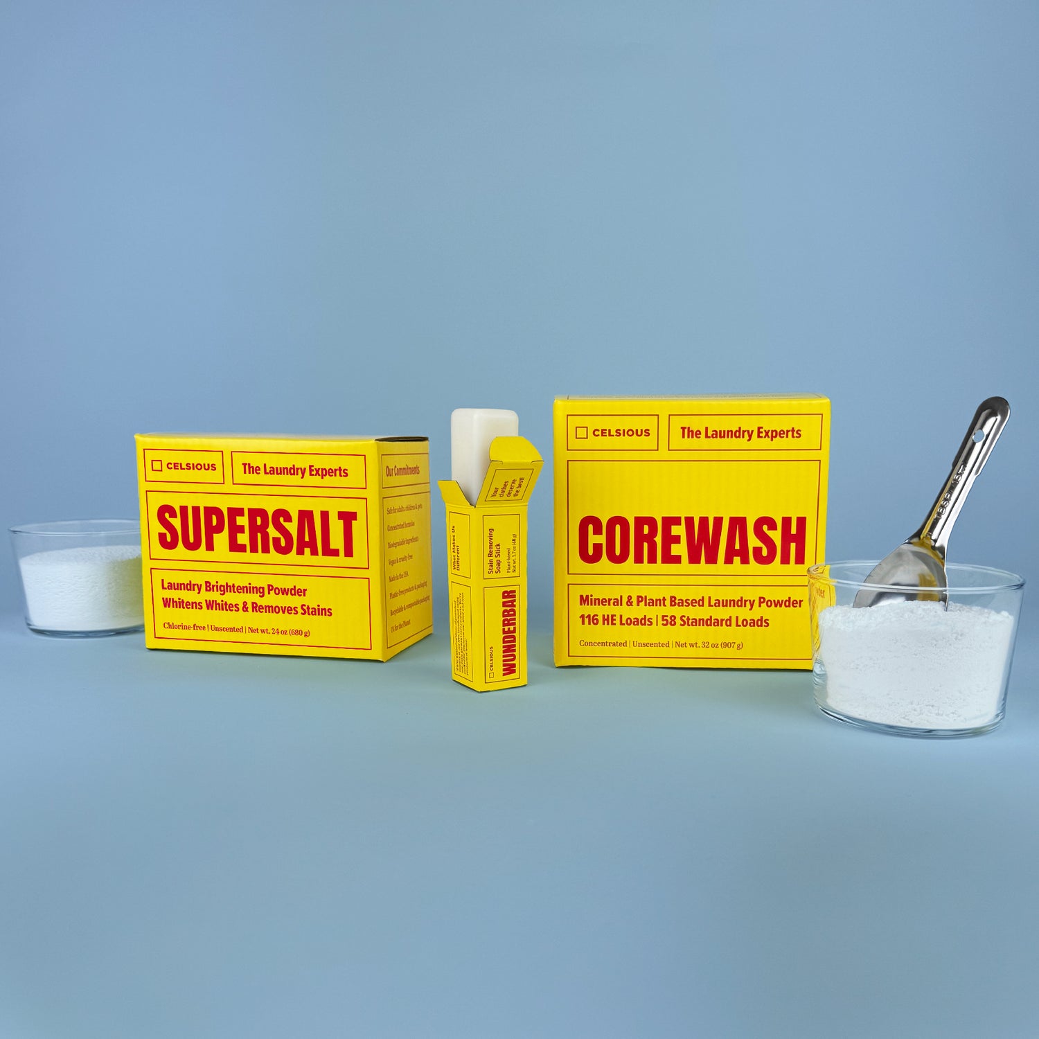 Corewash, Supersalt and Wunderbar in chic yellow packaging with red font, photographed with unpackaged laundry powders and a stain stick