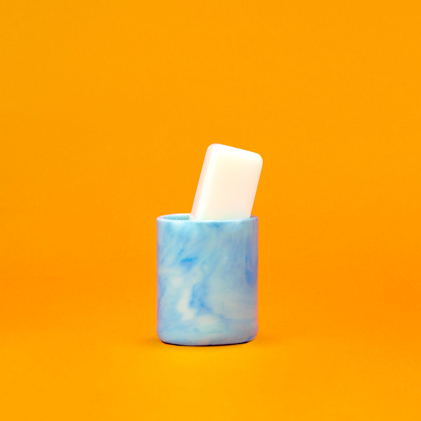 A stain removing soap stick sits at an angle in a small marble patterned ceramic holder