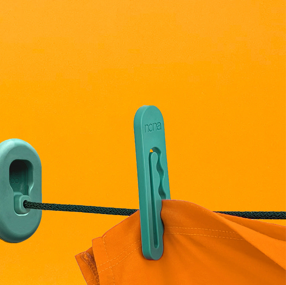 A green clothespin by NONA holds orange fabric on a green clothesline knit from recycled ocean plastic