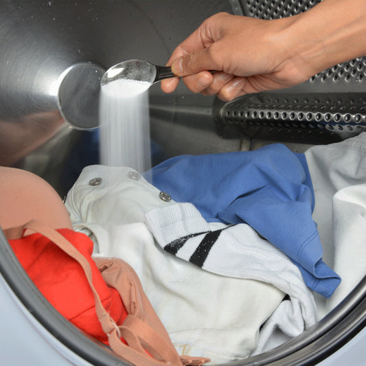 A scoop of laundry powder dispensed onto a load of laundry