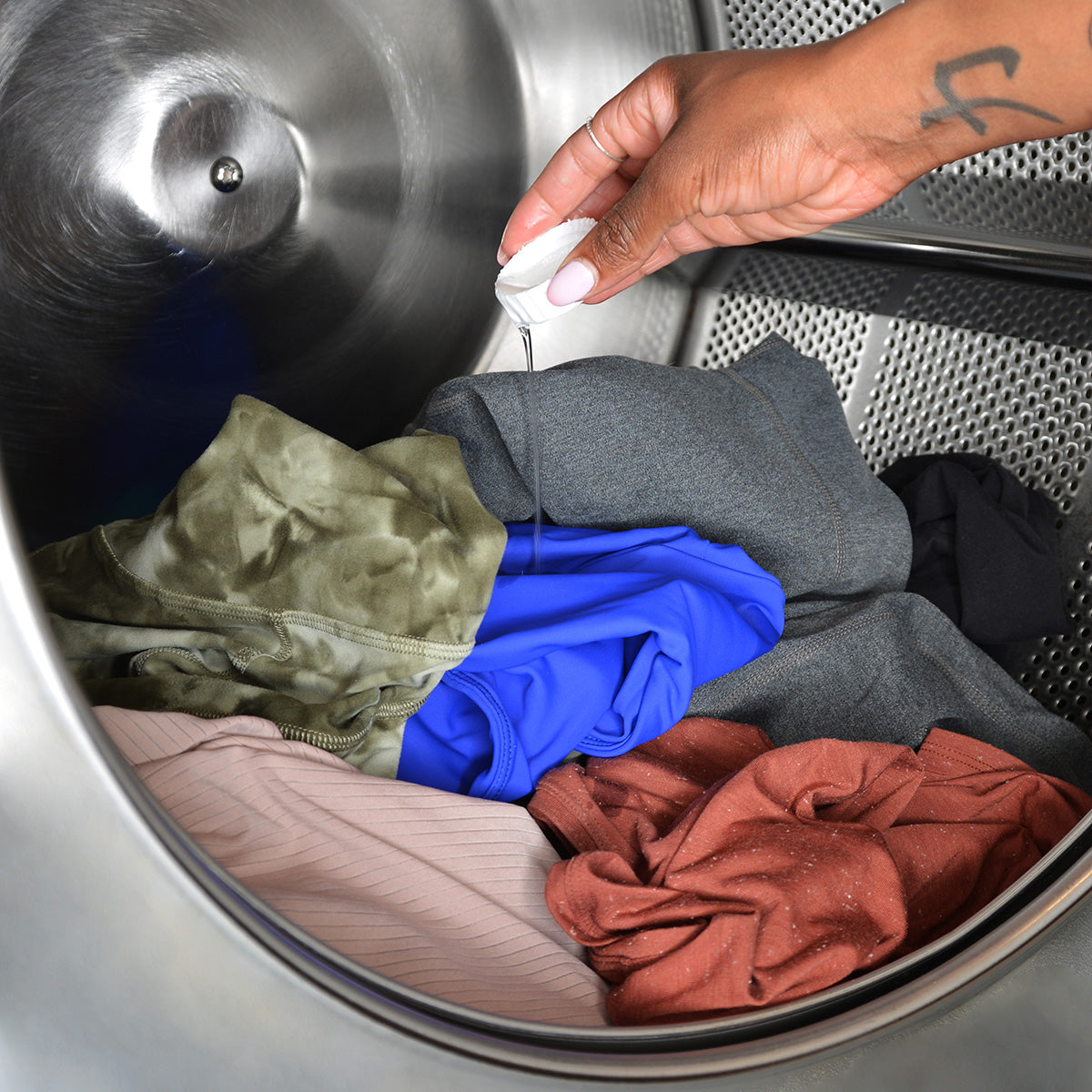 A hand pours a cap full of liquid detergent into the drum of a washing machine filled with sportswear
