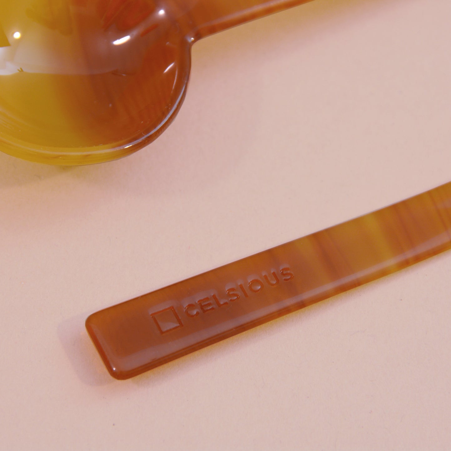 A close up shot of an orange and yellow sunset-like cellulose measuring spoon; the handle reads CELSIOUS