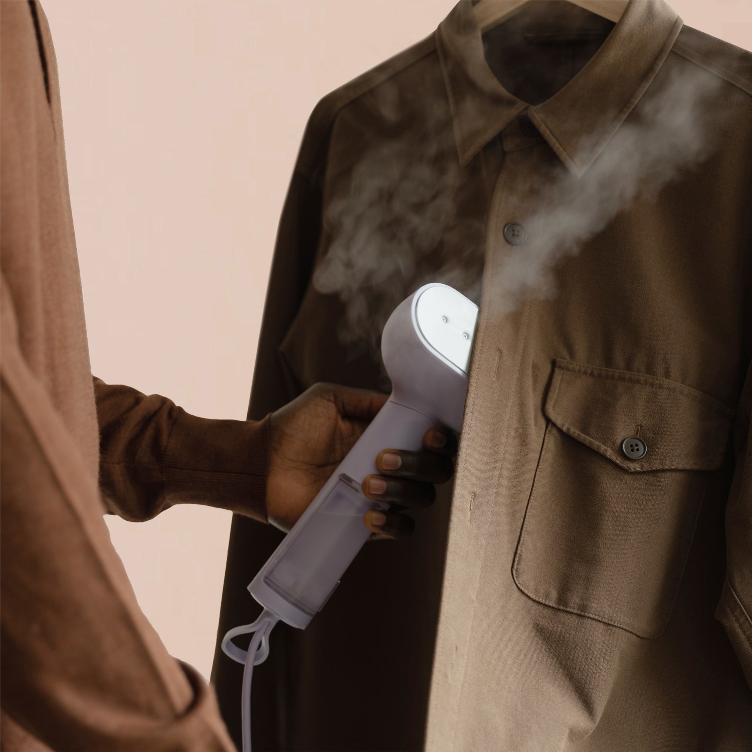 A man freshens up a brown shirt with a lilac steamer by Steamery