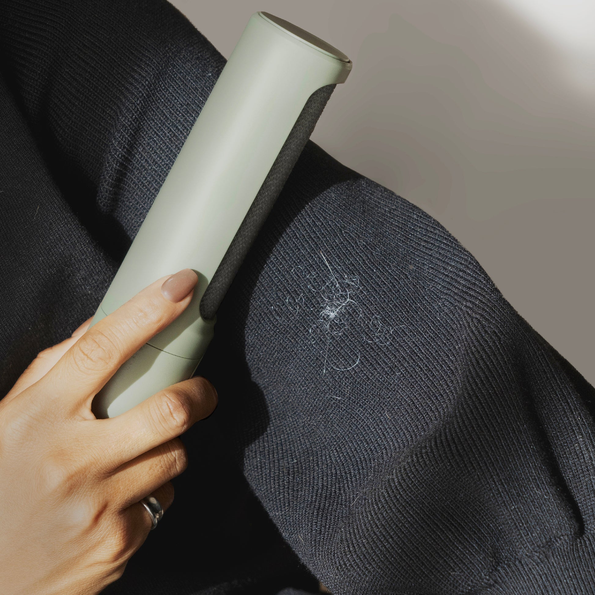 A hand holds up Steamery's chic lint lifter in sage next to a ball of lint