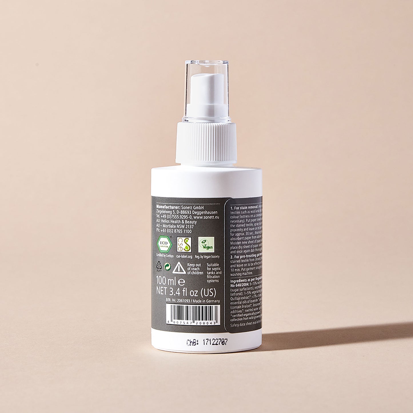 A white spray bottle of Sonett eco-friendly stain removal spray with a grey label stating usage instructions and certifications, displayed on a beige backdrop