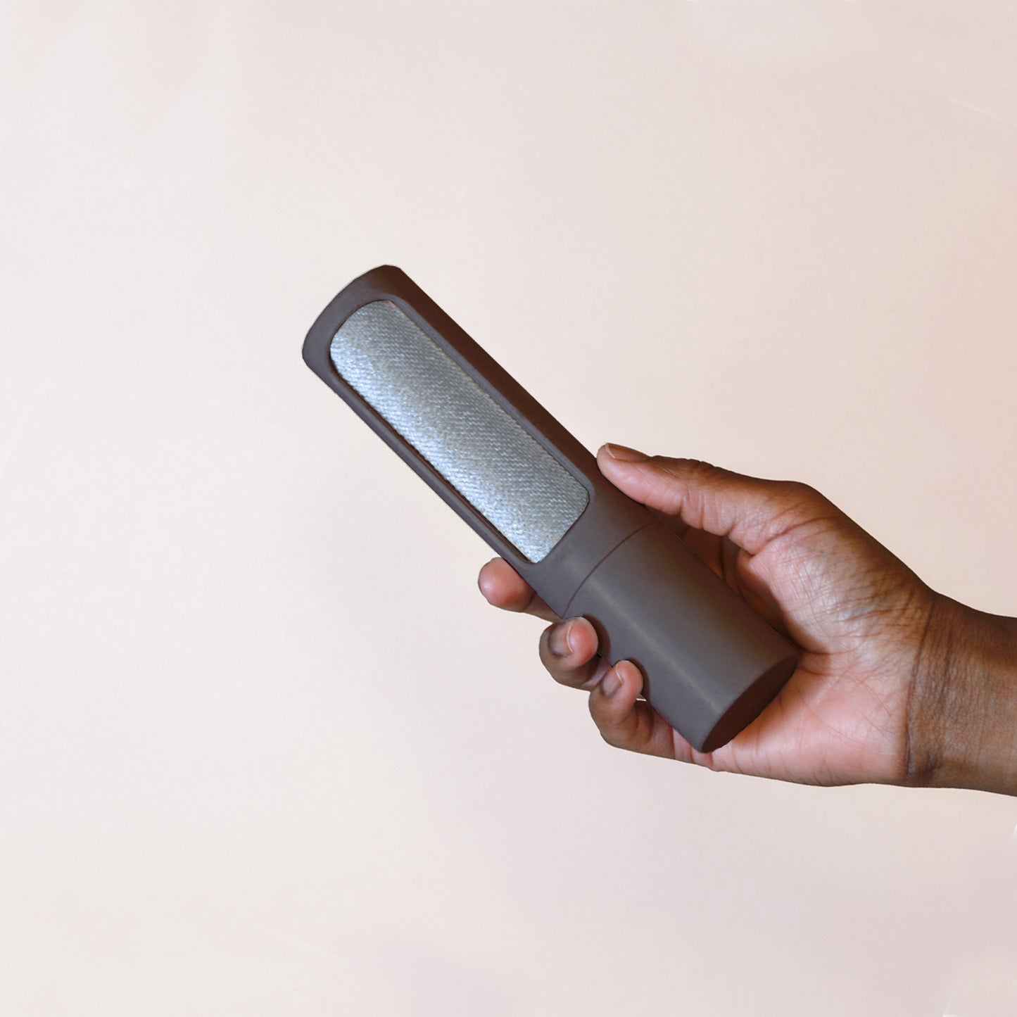 A hand holds a charcoal reusable lint roller in front of a beige backdrop