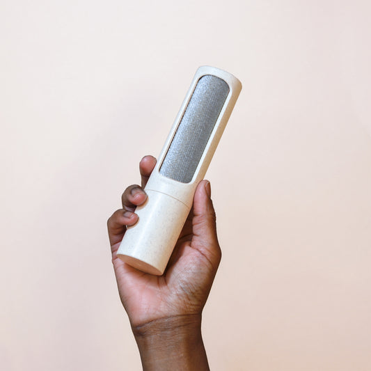 A hand holds a beige speckled reusable lint roller in front of a beige backdrop
