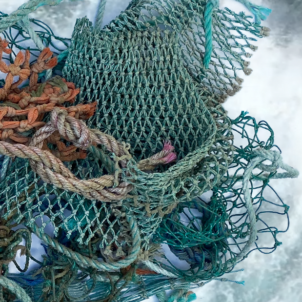 A pile of discarded fishing nets in different shades of green with hints of orange