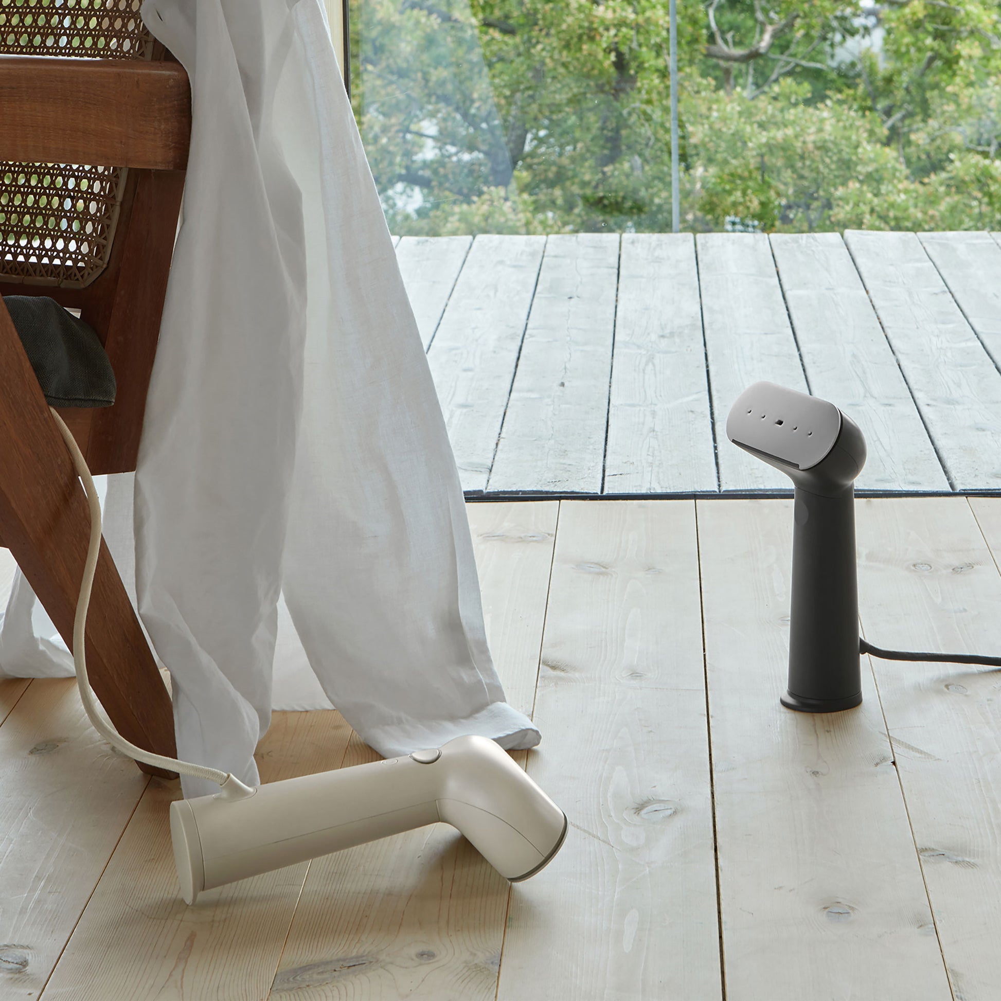 Two sleek devices can be seen on the wooden floor of a cottage – the black one is standing up and the light beige one is lying face down. These are dual function devices, used as both steamers and irons.
