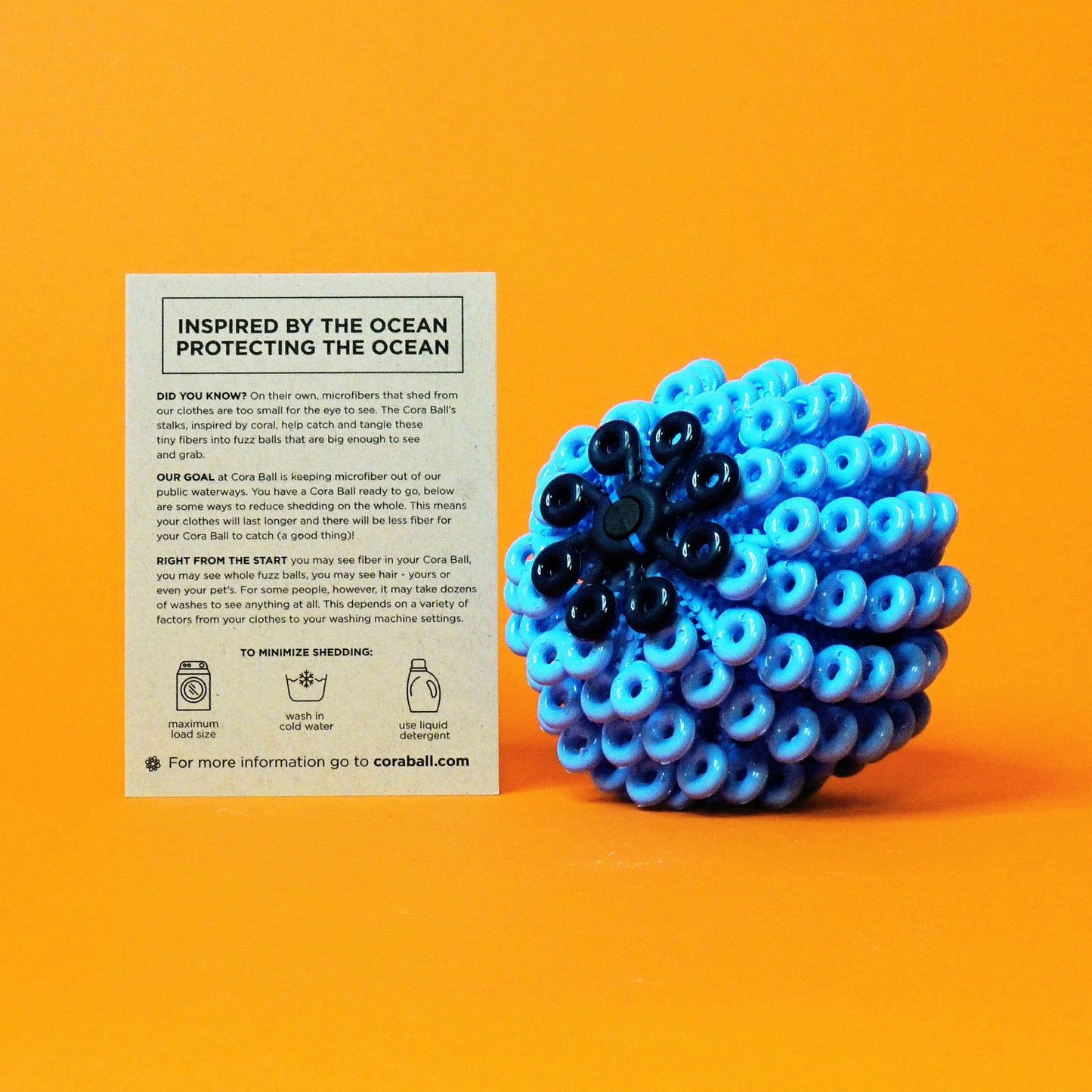 An avant-garde laundry ball used to catch microfibers displayed with an info card; the ball is blue with numerous loops, modeled after coral reef, and the backdrop is orange