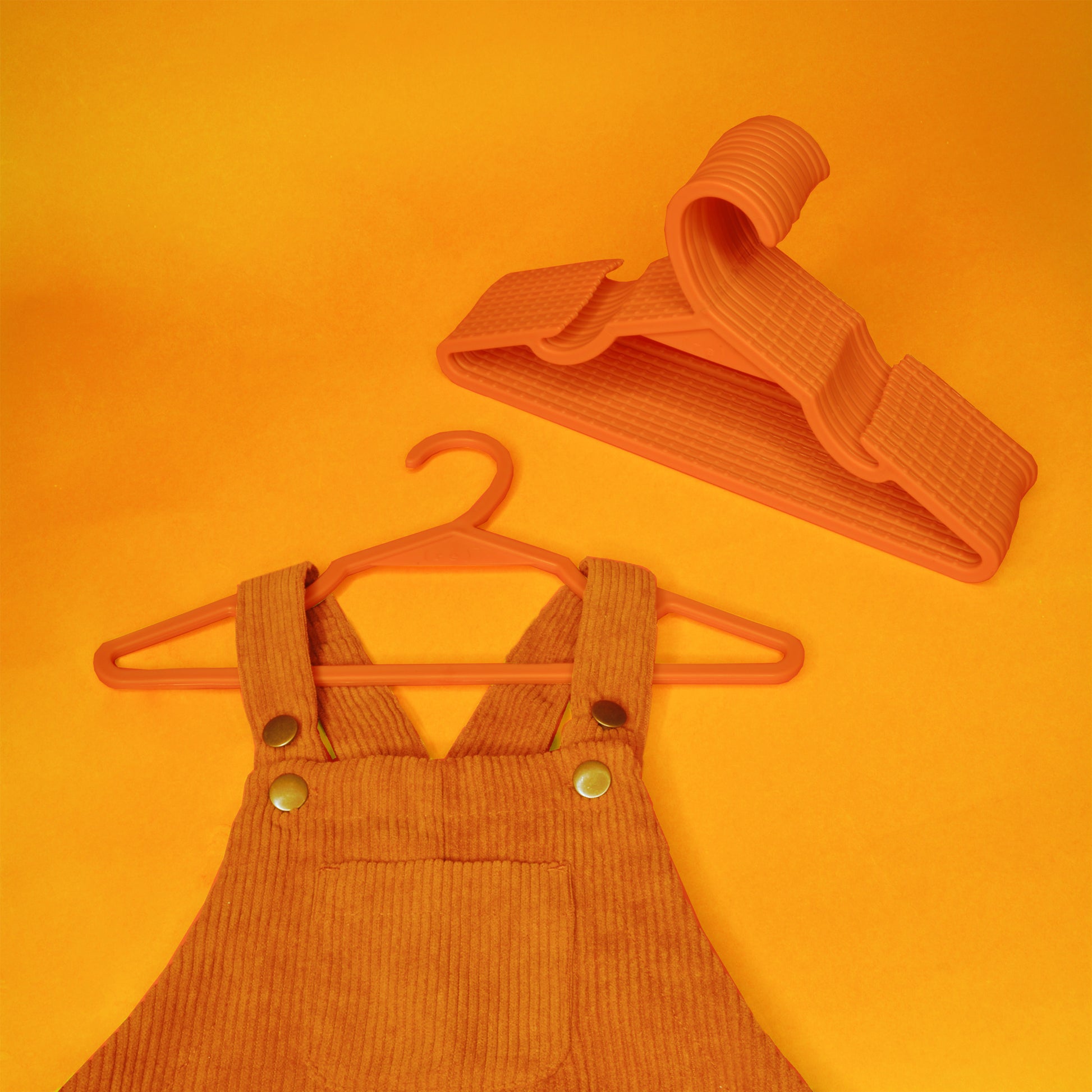 A toddler's corduroy overalls with a set of orange kids hangers made from recycled ocean plastic