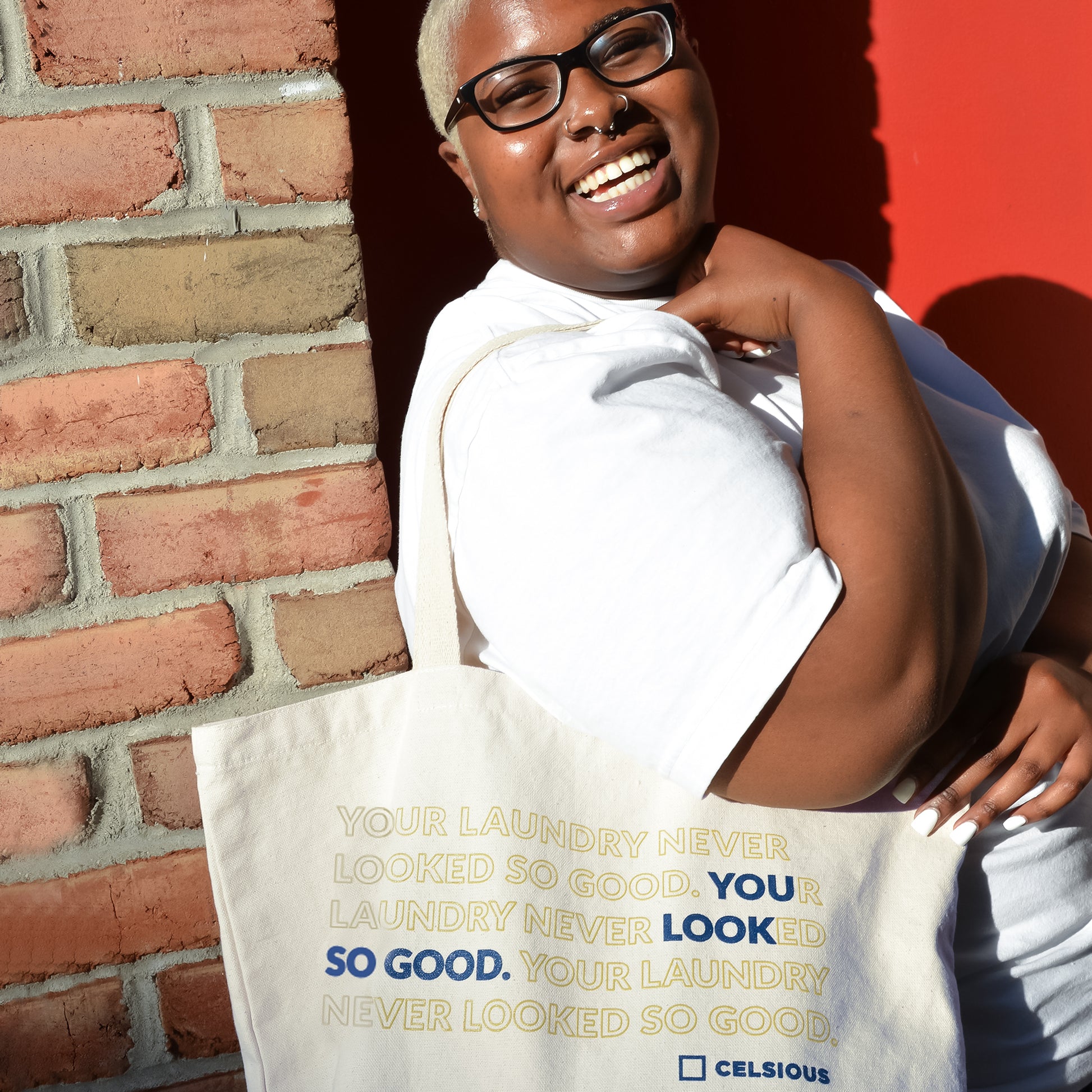 A young Black woman smiles widely for the camera with a Celsious canvas tote  over her shoulder