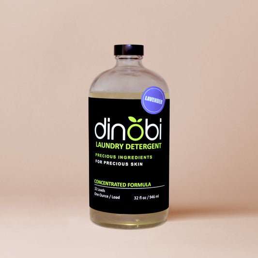 A glass bottle of Dinobi liquid laundry detergent with a black label and a round purple sticker with the word 'lavender'