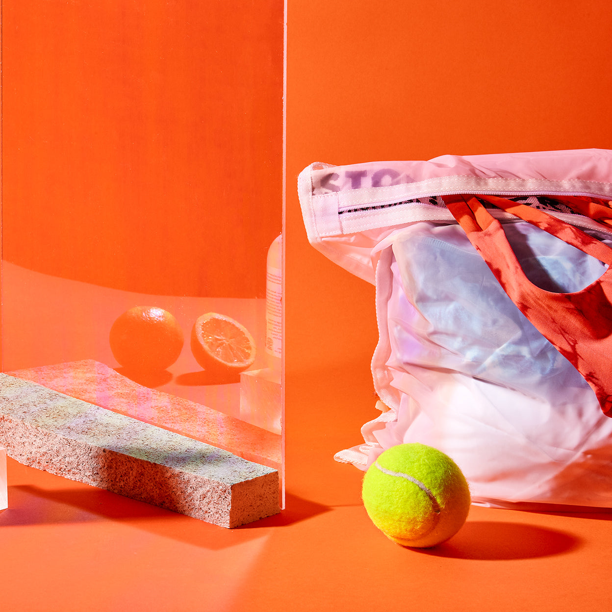 A Guppyfriend wash bag filled with laundry and a sportswear peeking out; to the side sits a tennis ball