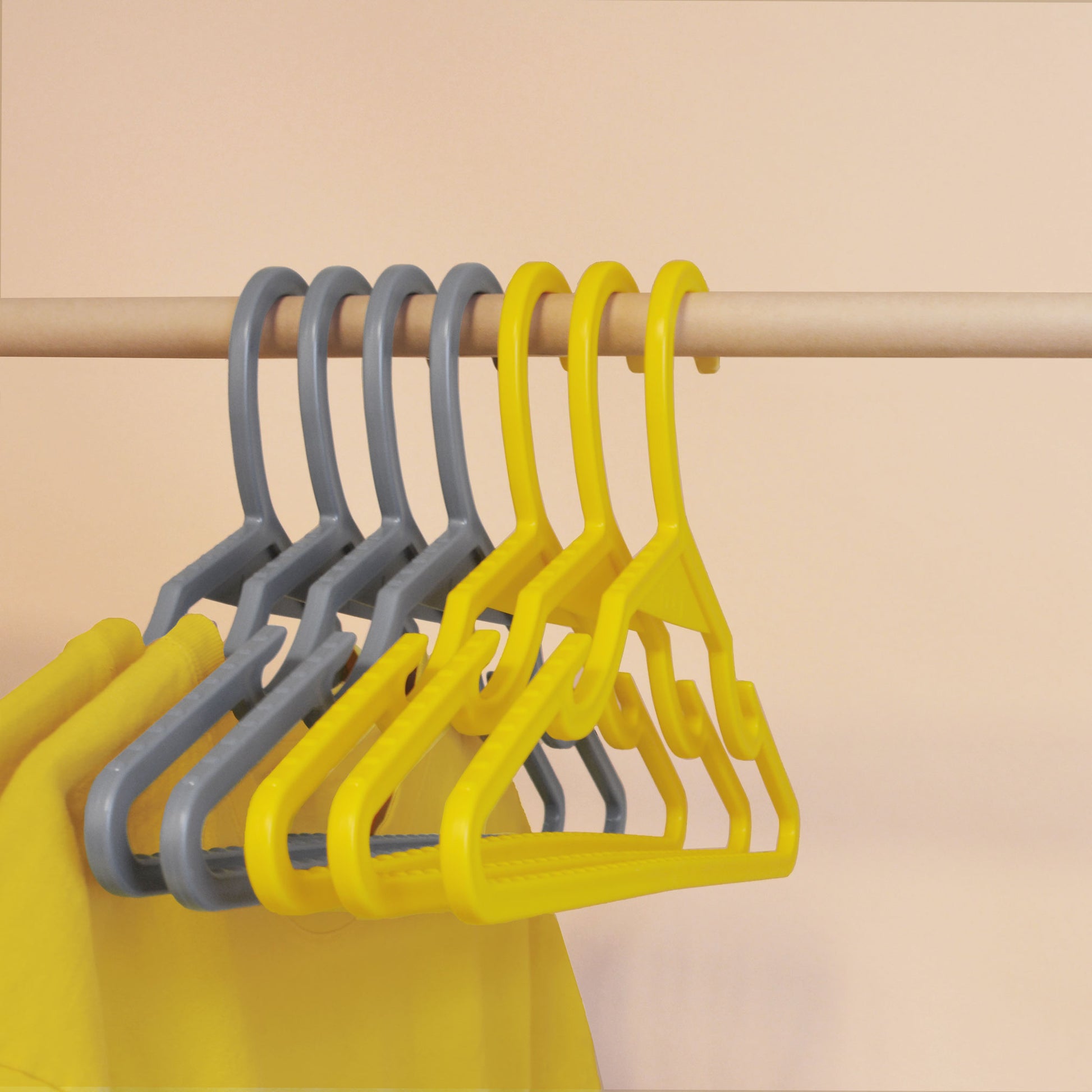 Grey recycled ocean plastic hangers on a wooden pole, with yellow t-shirts hanging from two of the four hangers; three empty yellow hangers hang in front