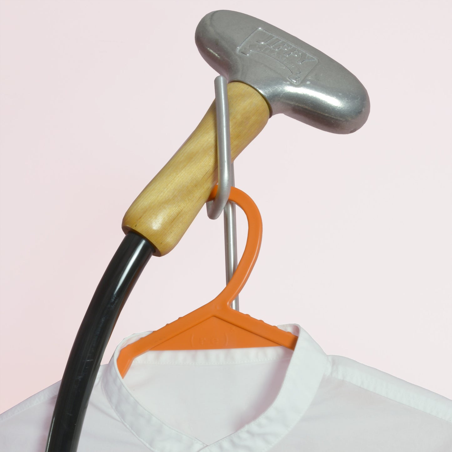 A close up of a Jiffy metal steam head perched on the built-in head rest; underneath is a white collarless shirt hanging from an orange hanger