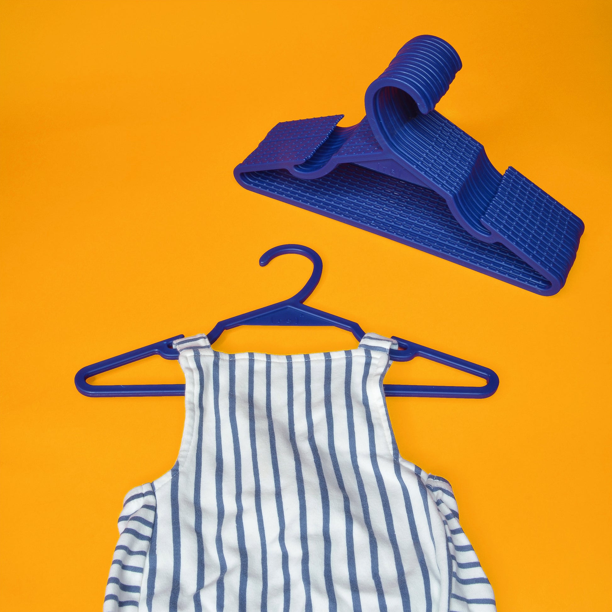 A toddler's navy striped overalls with a set of vibrant blue kids hangers made from recycled ocean plastic