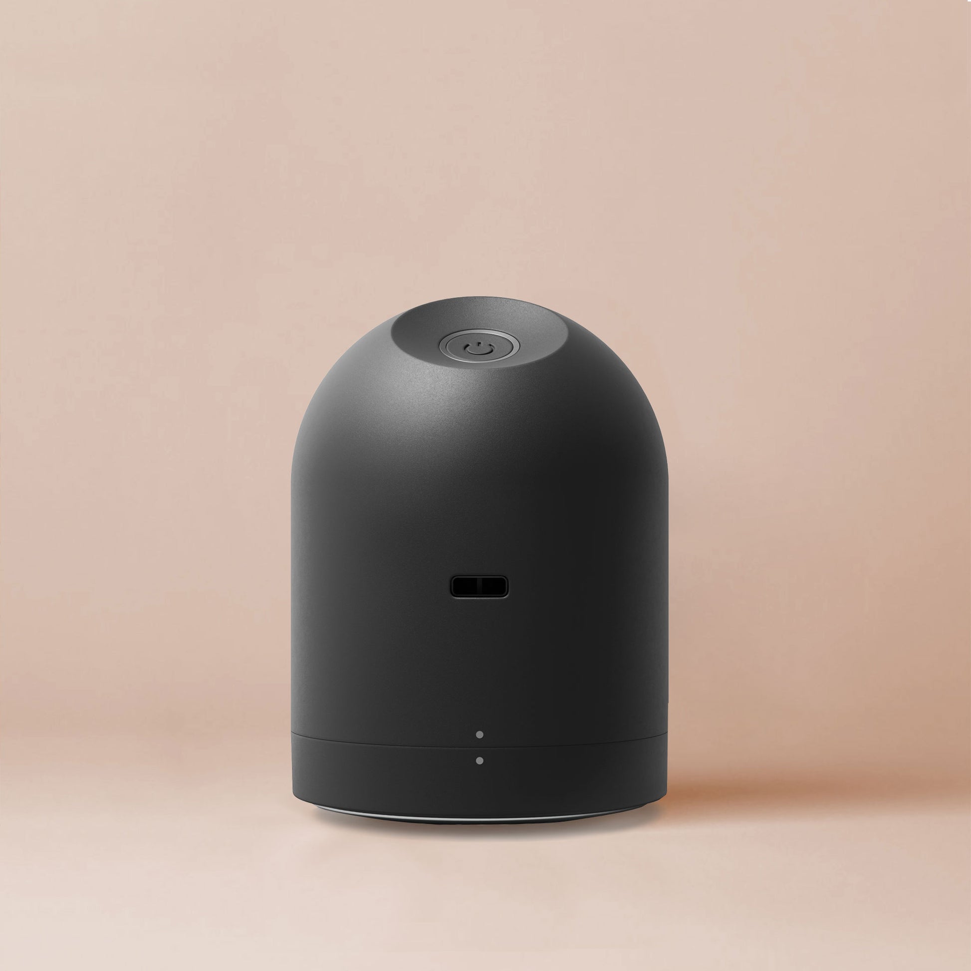 A sleek dome shaped charcoal fabric shaver is displayed on a beige background; a power button and a hole for the USB charger can be seen on the device from this angle